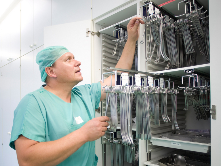 Mitarbeiter hängt OP-Besteck in einen Schrank - Zentrale Sterilgutversorgungsabteilung Mitarbeiter hängt OP-Besteck in einen Schrank - Zentrale Sterilgutversorgungsabteilung